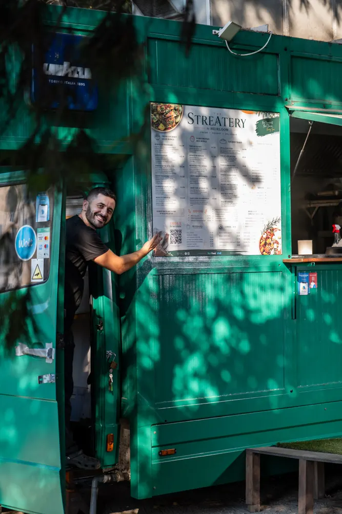 A team member at The Streatery truck pointing to the menu board